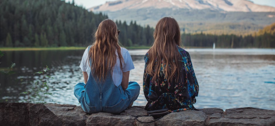 two girls sitting near lake